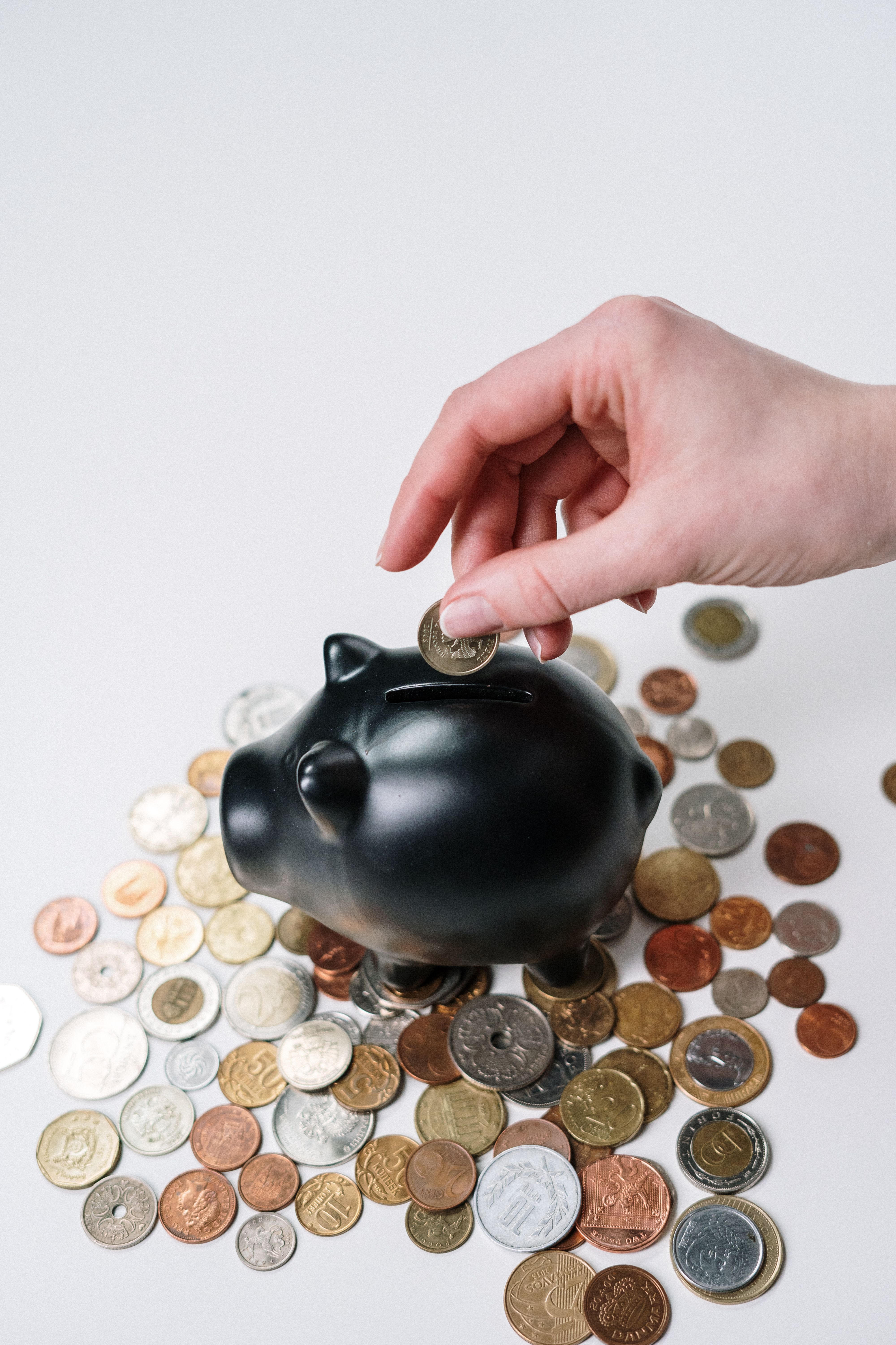 Hand inserting a coin into a piggy bank among scattered coins, symbolizing retirement savings
